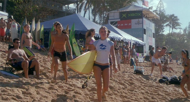 砂浜でサーフボードを持って歩くアン・マリー